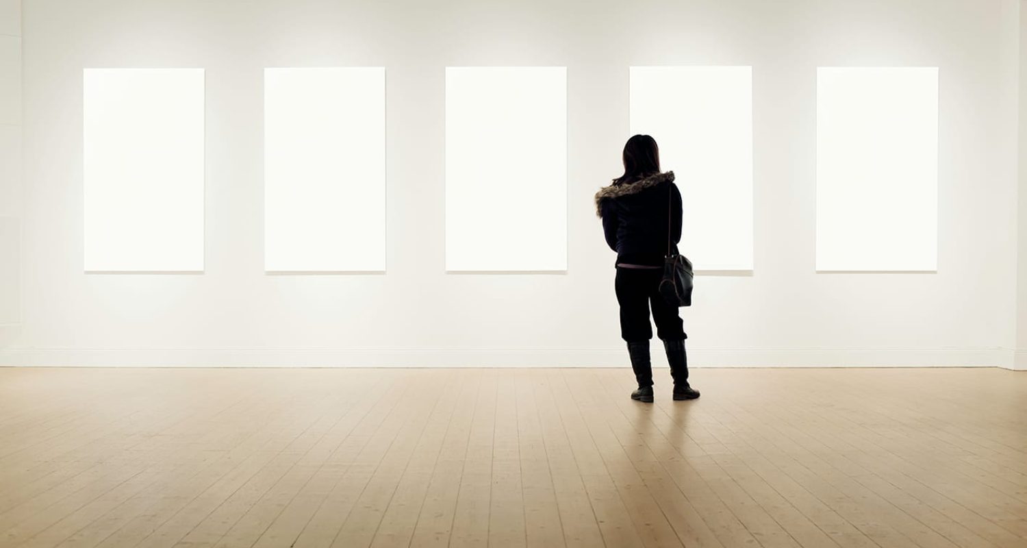 Woman visits art exhibition with several works on display. Clipping path included for the blank frames.