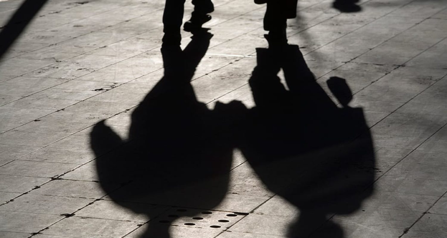 sun casting shadow over two people walking on the street
